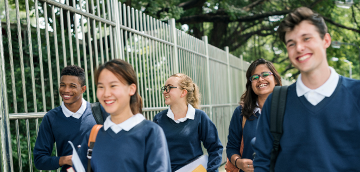 Group of 5 teenagers in school uniform walking together, smiling and talking.