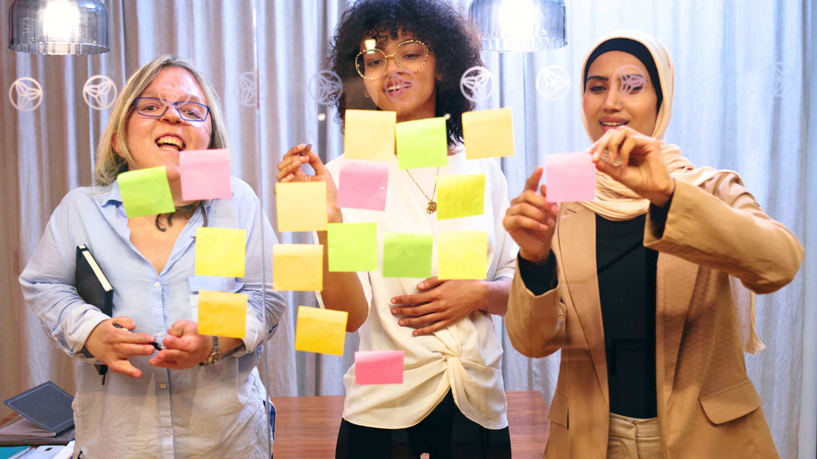 3 women placing post-it notes on a glass pane