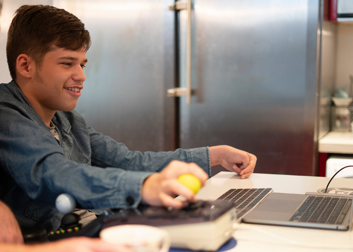 A teenage boy with a disability, sitting in a wheelchair using a laptop