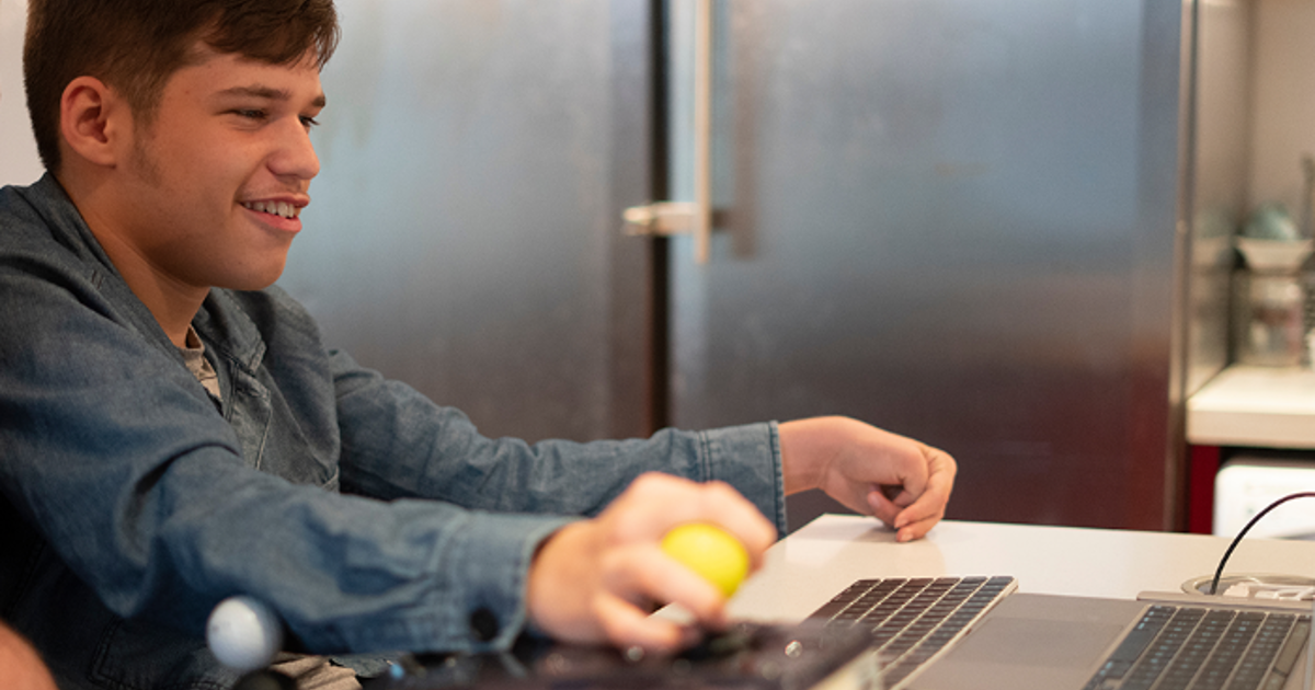 A teenage boy with a disability, sitting in a wheelchair using a laptop
