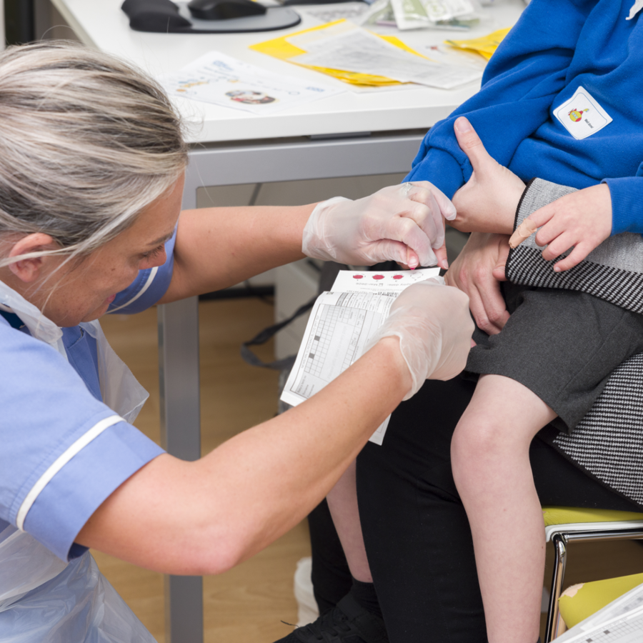 Nurse Examining Child Sat On Parents Lap