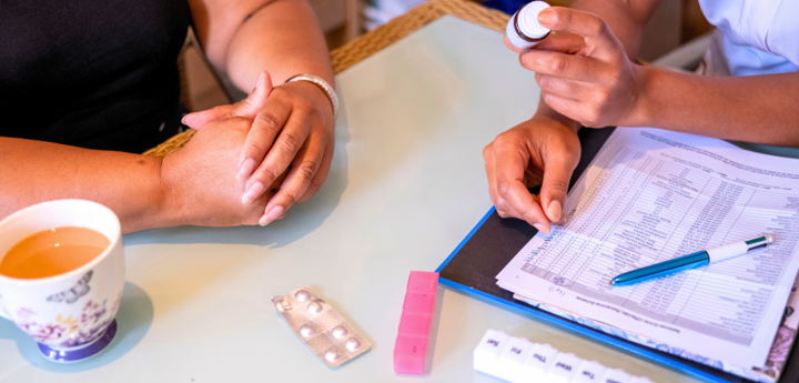 Nurse showing a bottle of medication to a patient at their dining room table.