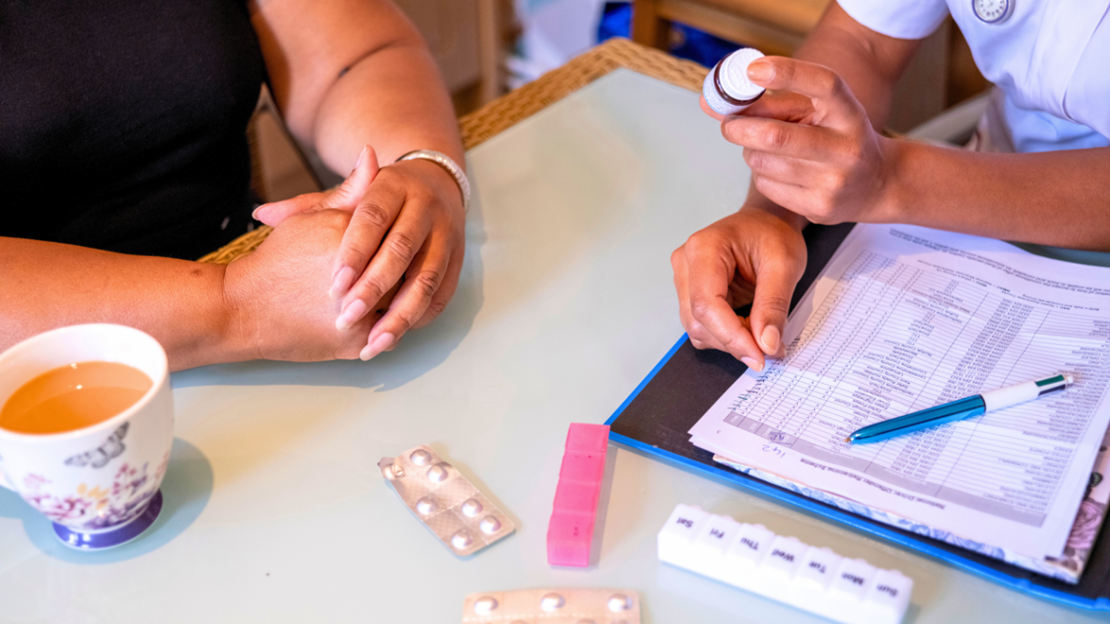 Nurse showing a bottle of medication to a patient at their dining room table.