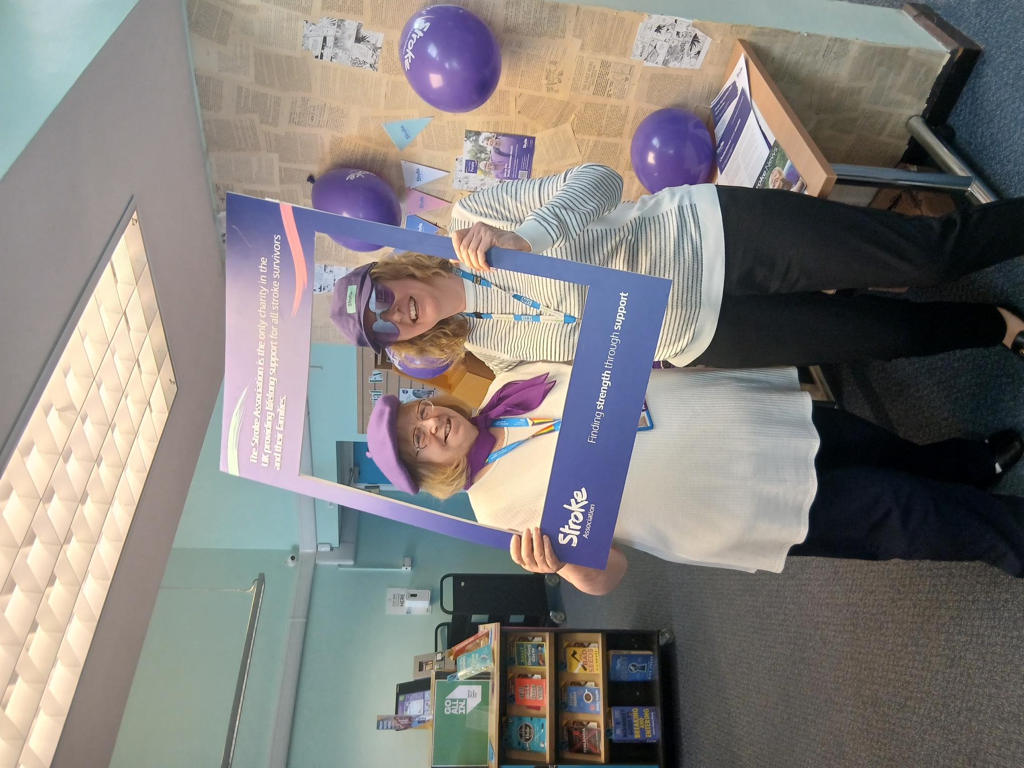 A photo of two smiling NHS workers holding up a purple photo frame that promotes the Stroke Association charity