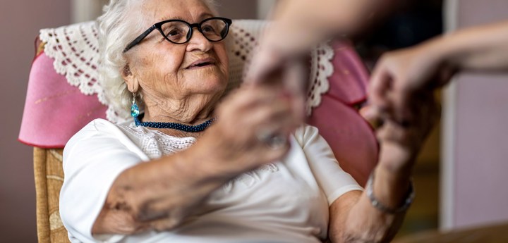 Elderly woman being assisted to stand up from her armchair
