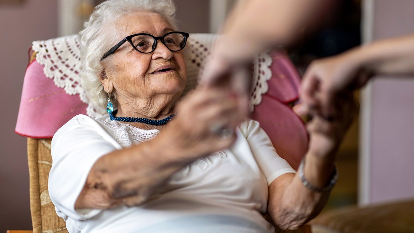 Elderly woman being assisted to stand up from her armchair