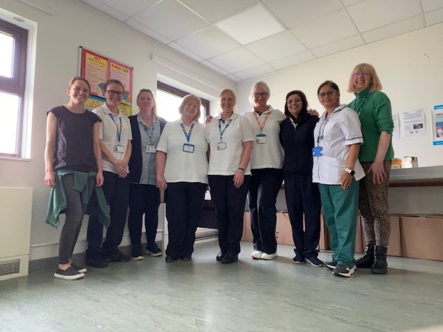 A photo of a group of female NHS workers, some are wearing medical scrubs. They are all smiling into the camera