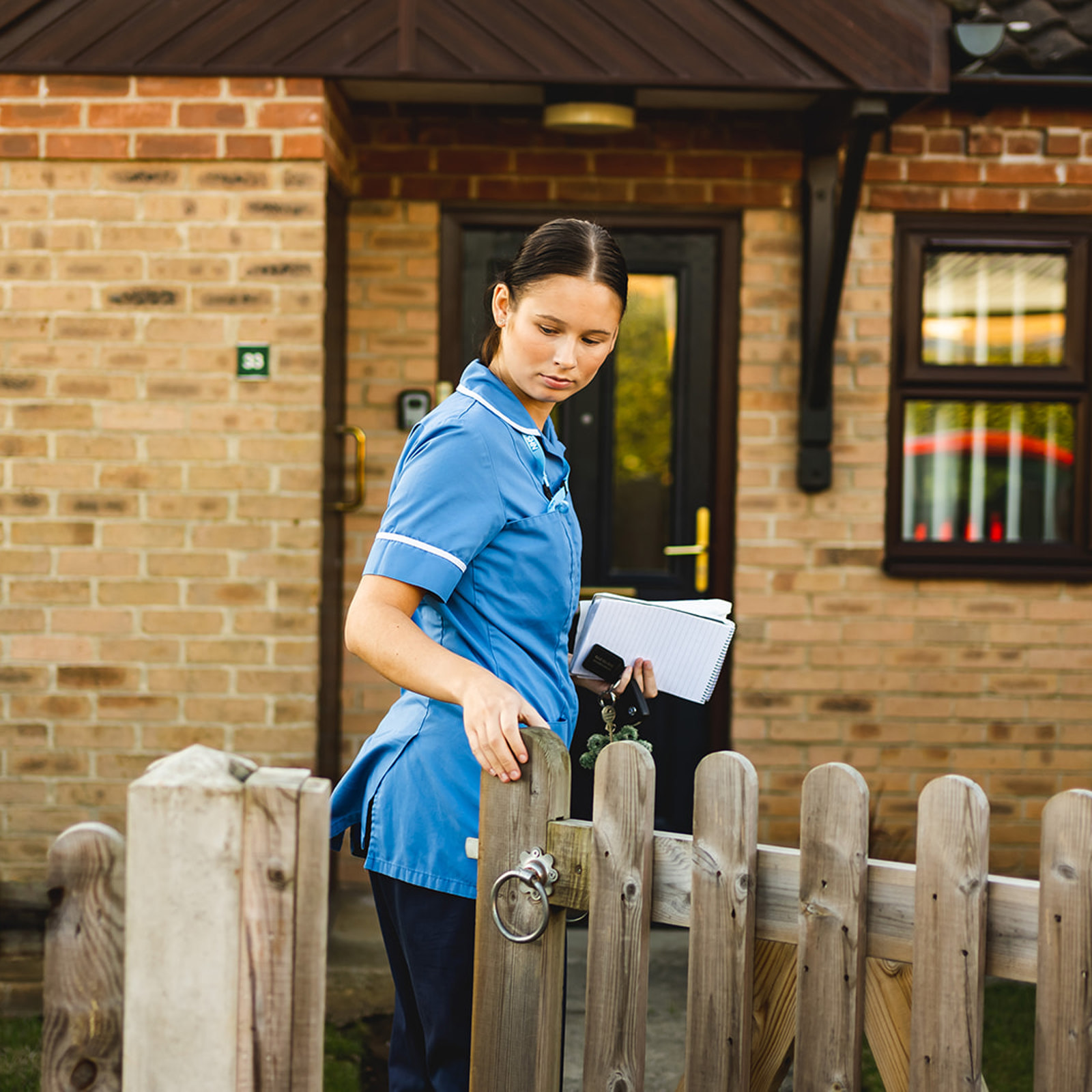 Community nurse closing a gate behind them as they approach a home.