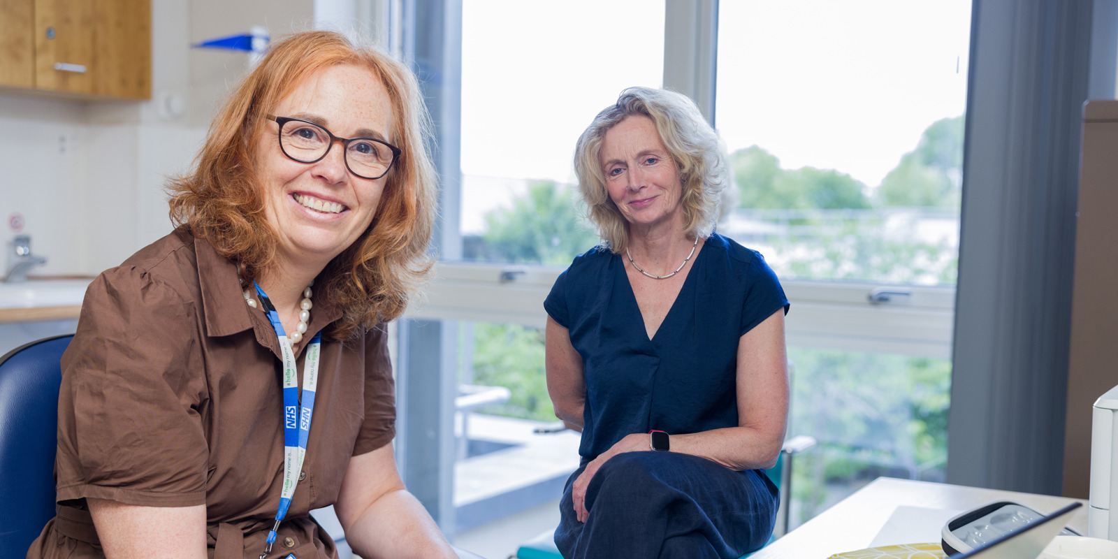 Two women sitting in a clinical room smiling at the camera 