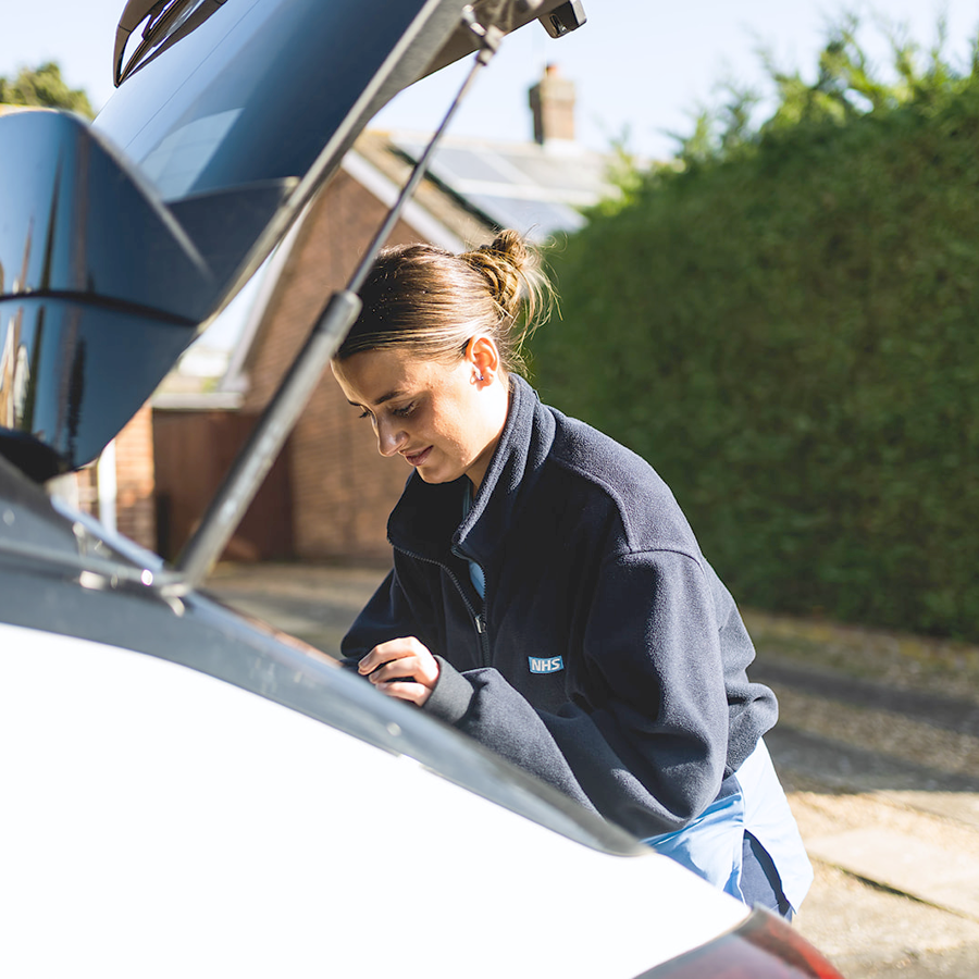 Nurse looking into boot of a car during home visit