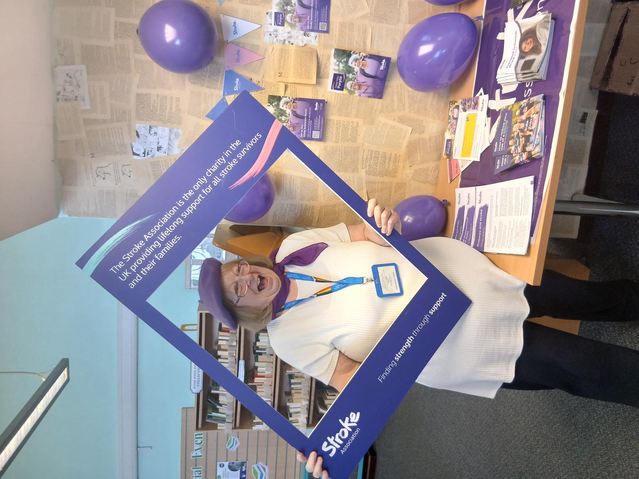 A laughing NHS worker holding up a frame that promotes the Stroke Association charity