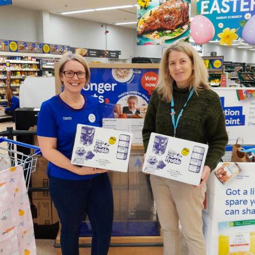 Tesco staff member and Trust staff member holding boxes of Freddo Easter eggs