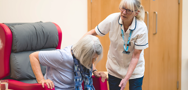 Clinician helping older woman to stand up from armchair