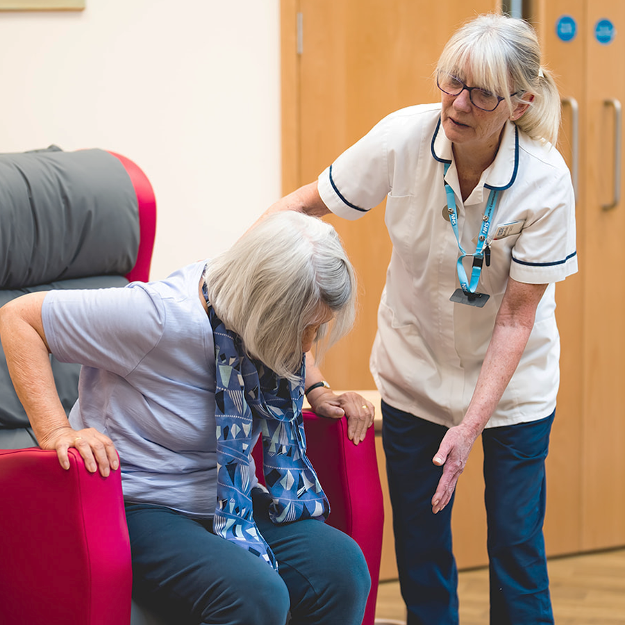 Clinician helping older woman to stand up from armchair