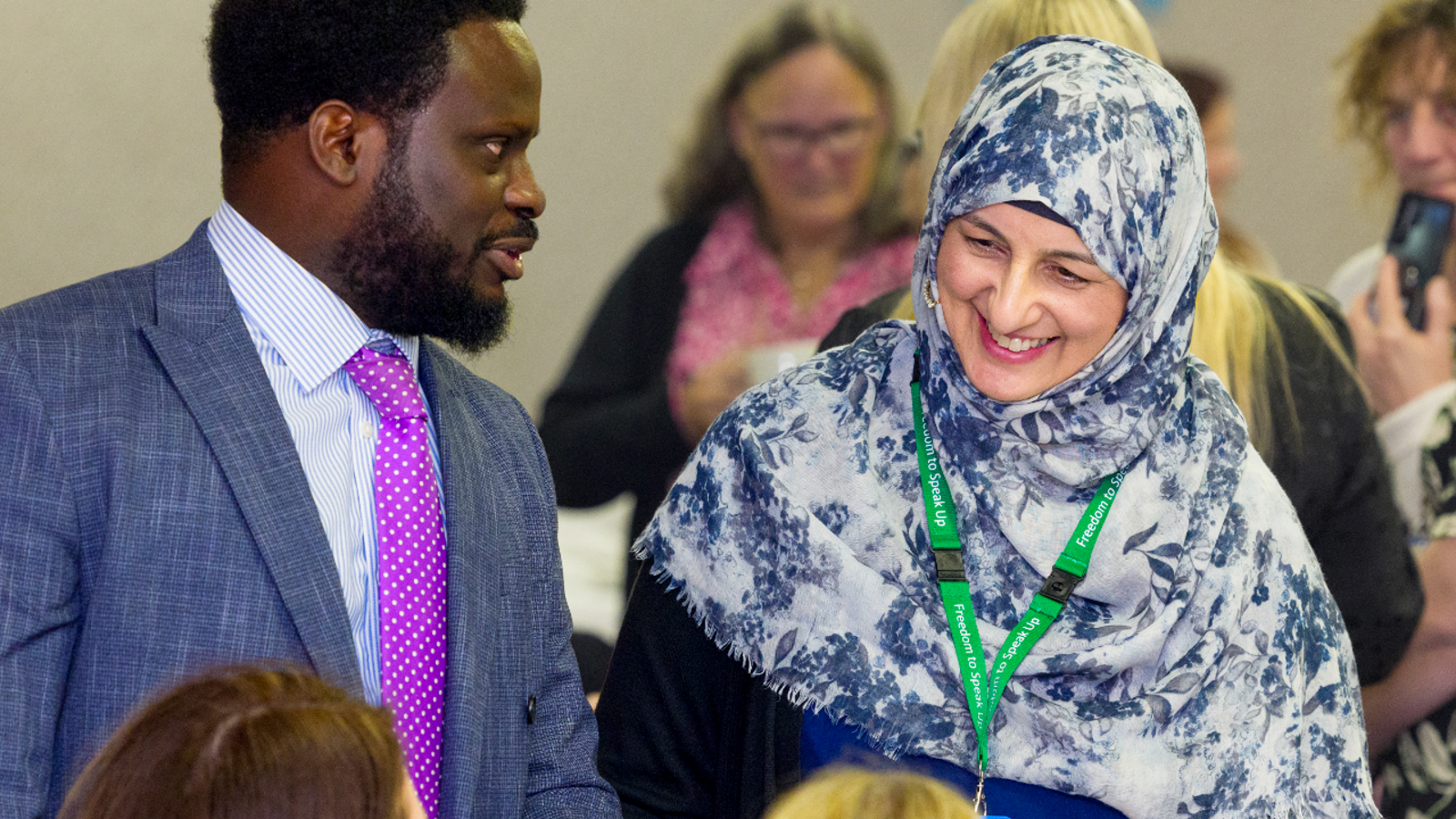 Black man in a suit and woman in hijab talking and laughing at conference.