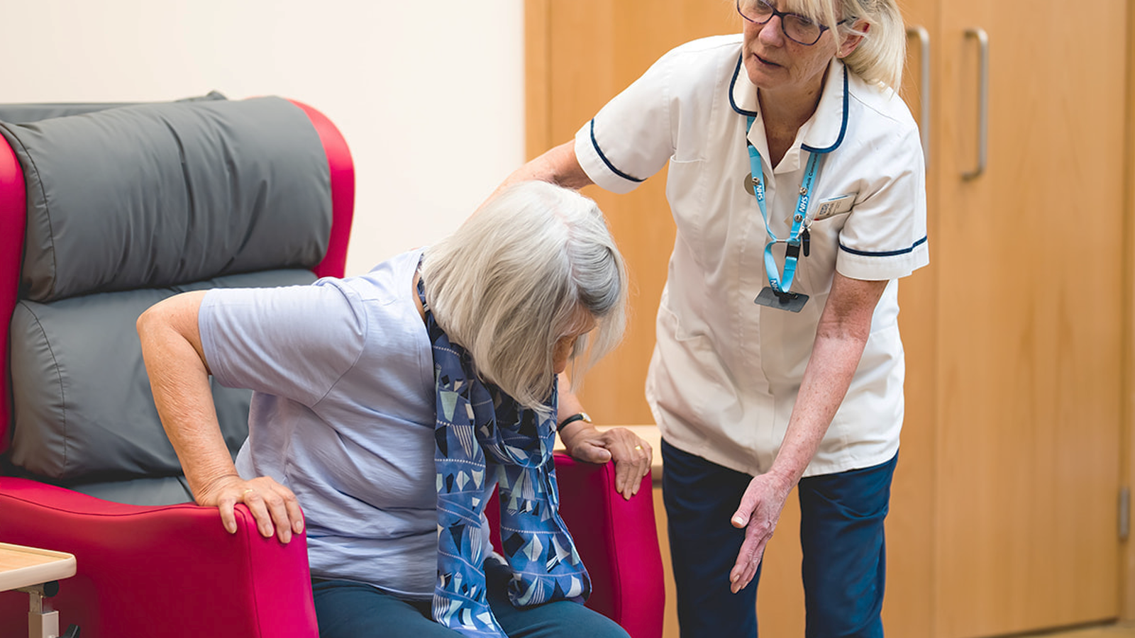 Clinician helping older woman to stand up from an armchair.