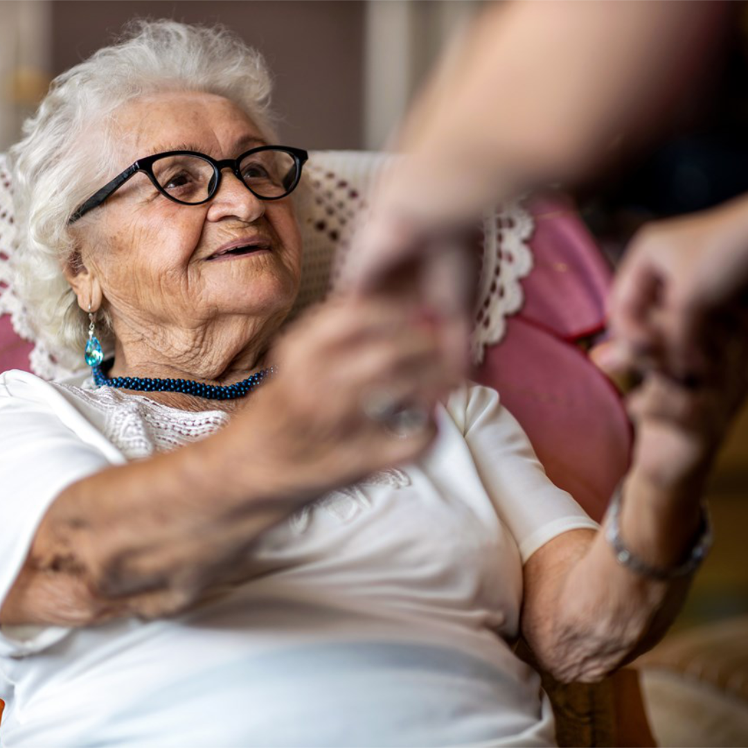 Elderly woman being assisted to stand up from her armchair