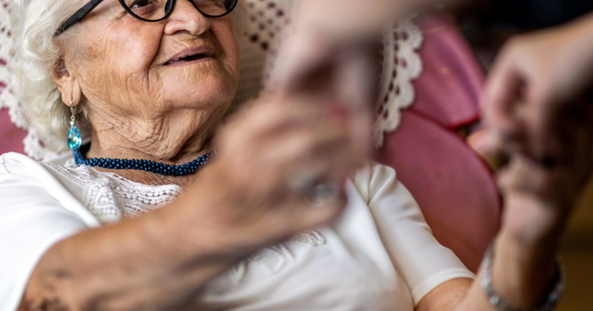 Elderly woman being assisted to stand up from her armchair