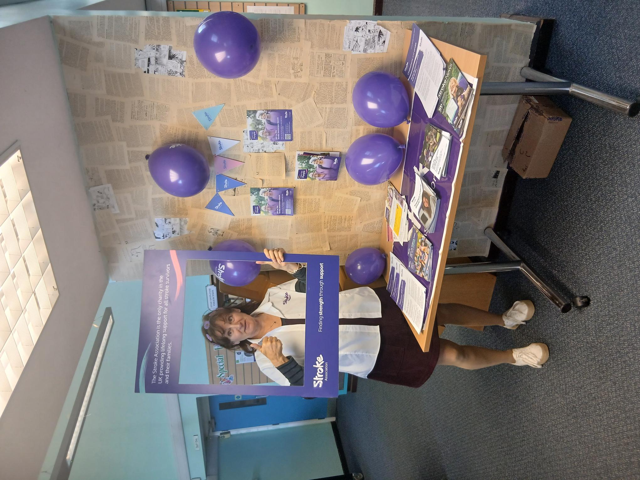 A photo of an NHS worker giving a thumbs up and holding a purple photo frame that promotes the Stroke Association charity