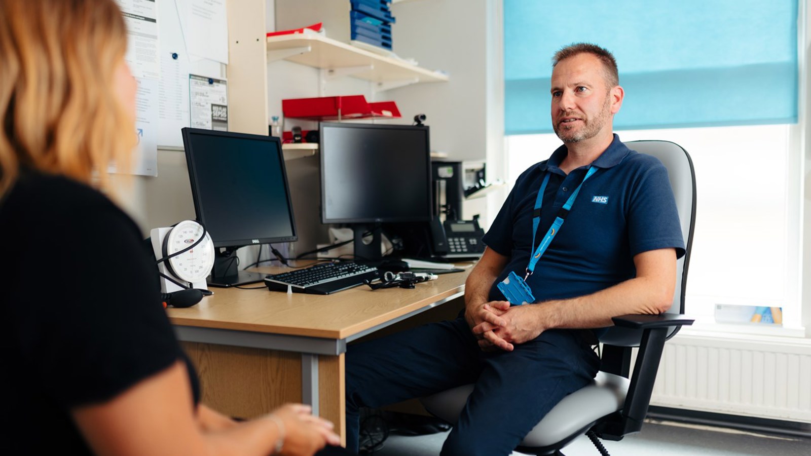 GP sitting in chair at a desk, speaking to a patient