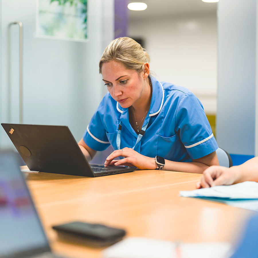 Nurse sitting at a table looking at a laptop.