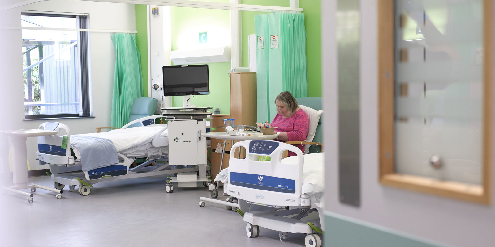Image of a service user at the Willow Therapy unit next to one of the new beds. They are wearing a pink shirt and eating in the sunlight.