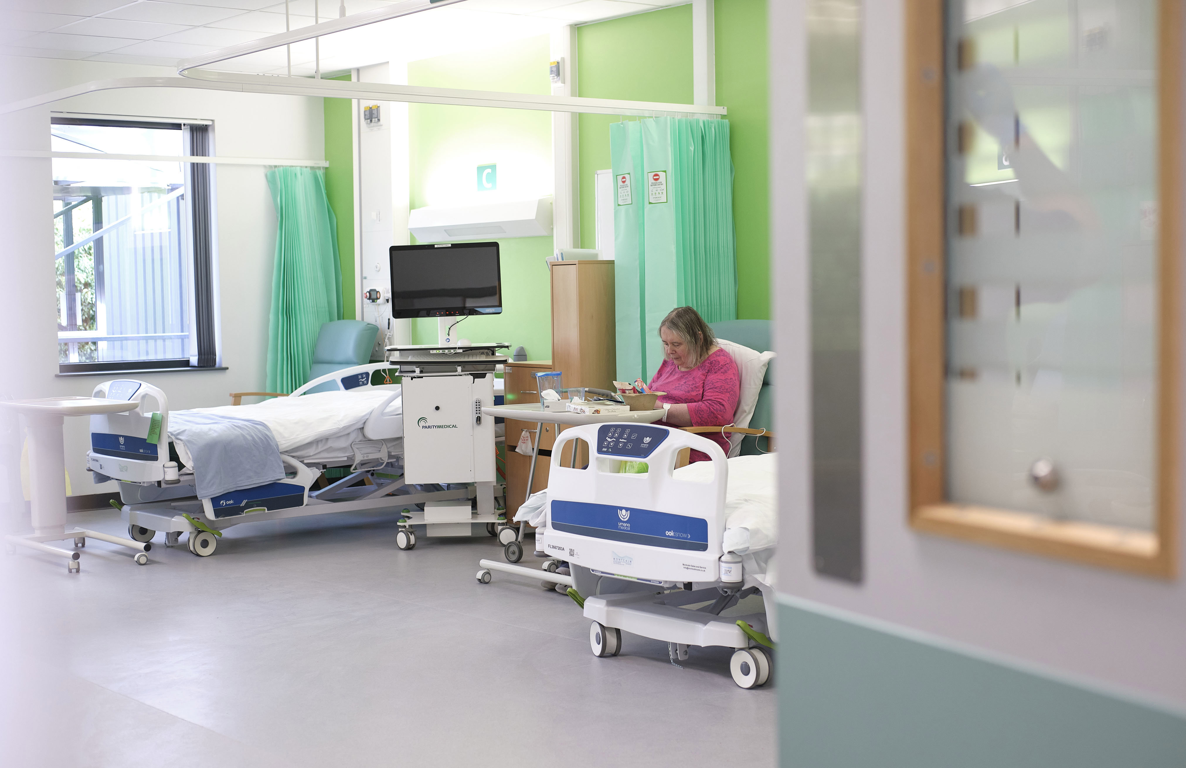 Image of a service user at the Willow Therapy unit next to one of the new beds. They are wearing a pink shirt and eating in the sunlight.