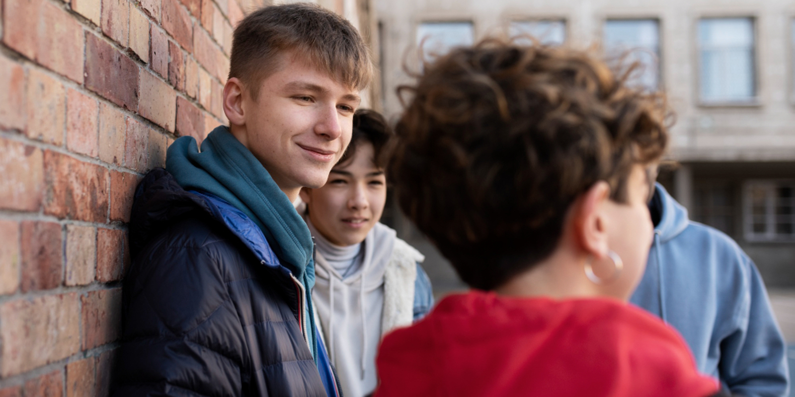Four teenagers standing next to a brick wall talking to each other