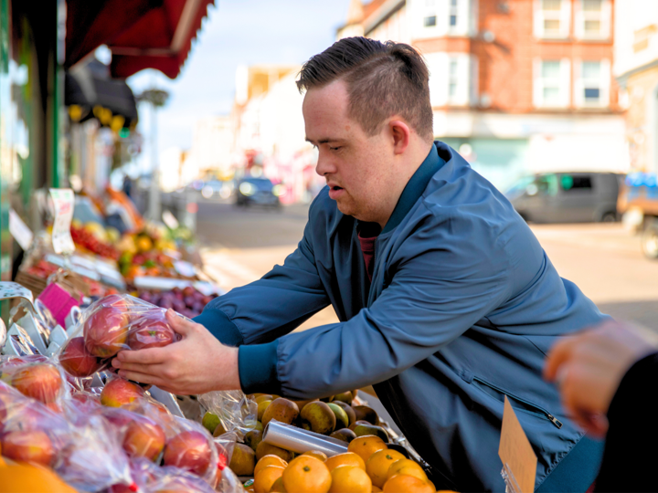 Young disabled man buying apples outside a grocery shop