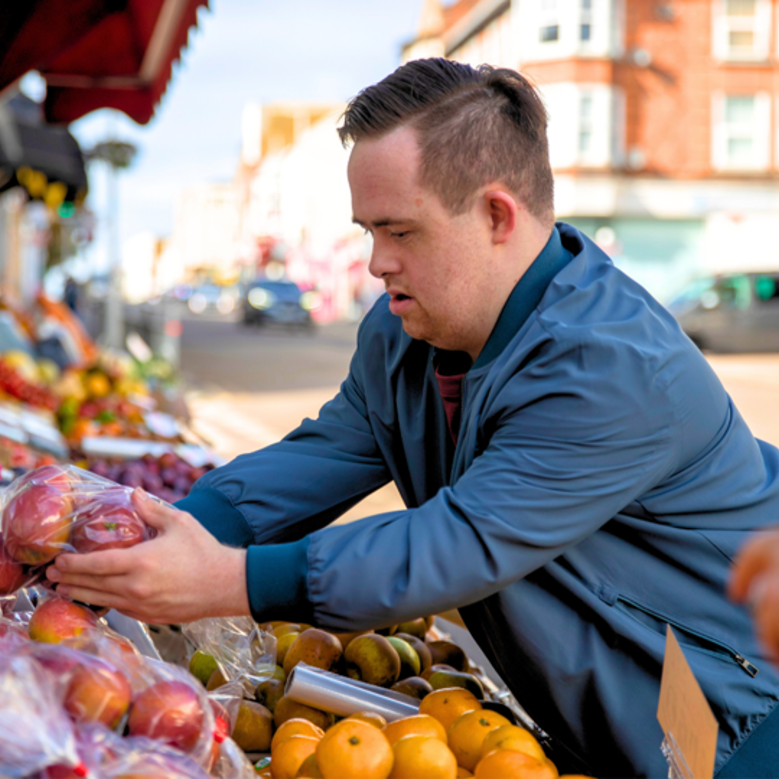 Young disabled man buying apples outside a grocery shop