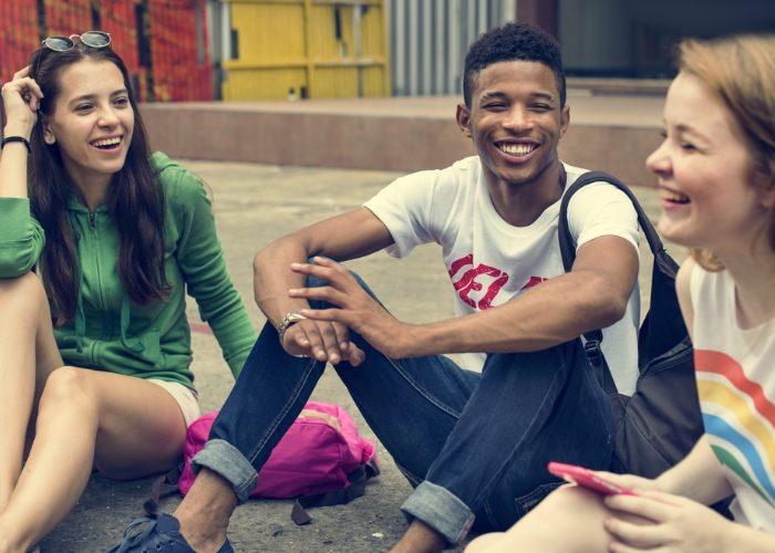 Three teenagers sitting on the ground laughing with each other